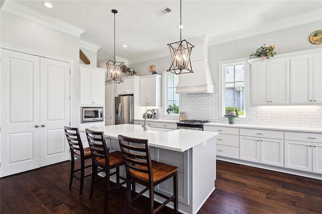 kitchen with backsplash, stainless steel appliances, a kitchen island with sink, white cabinets, and hanging light fixtures