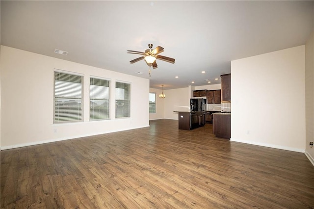 unfurnished living room with ceiling fan with notable chandelier, dark wood-type flooring, and a wealth of natural light