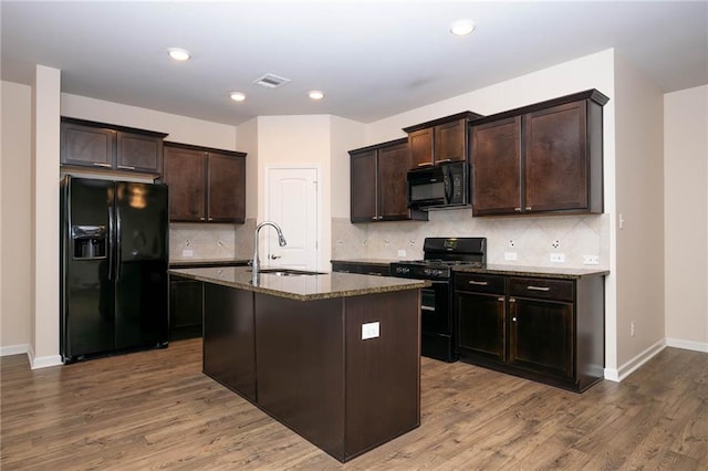 kitchen featuring hardwood / wood-style floors, black appliances, sink, an island with sink, and dark brown cabinetry