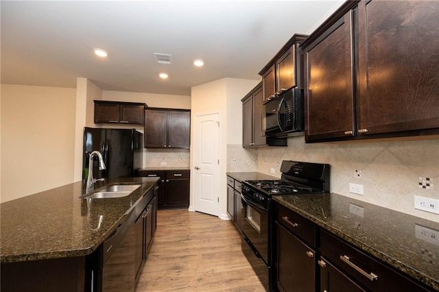 kitchen featuring decorative backsplash, sink, black appliances, dark stone countertops, and light hardwood / wood-style floors