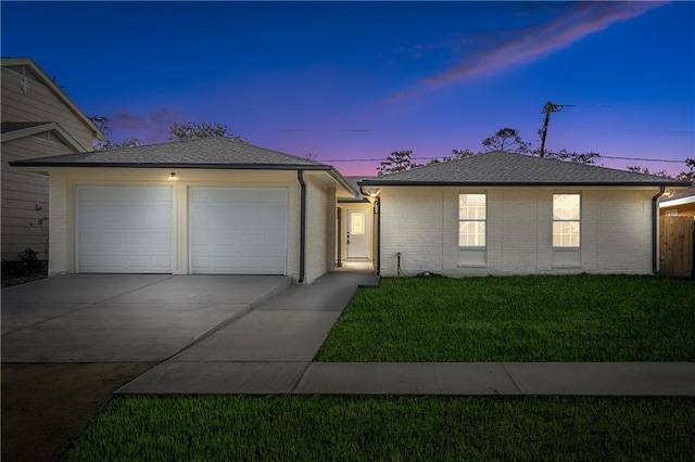 single story home featuring a shingled roof, concrete driveway, brick siding, and a yard