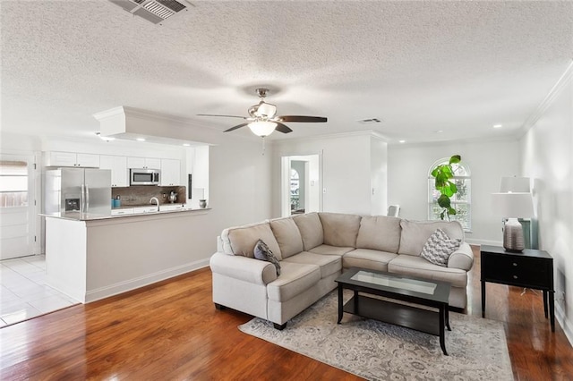 living room with sink, crown molding, light hardwood / wood-style flooring, ceiling fan, and a textured ceiling