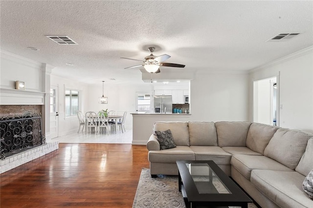 living room featuring crown molding, a brick fireplace, ceiling fan, a textured ceiling, and wood-type flooring