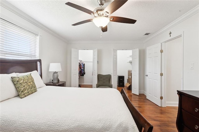 bedroom featuring ceiling fan, a spacious closet, dark hardwood / wood-style floors, crown molding, and a textured ceiling