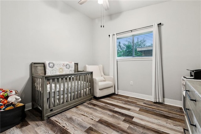 bedroom featuring ceiling fan, dark hardwood / wood-style floors, and a crib