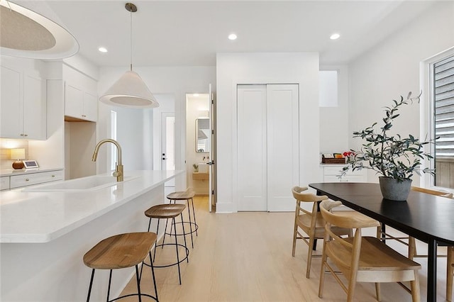 kitchen featuring white cabinets, light hardwood / wood-style floors, sink, and hanging light fixtures