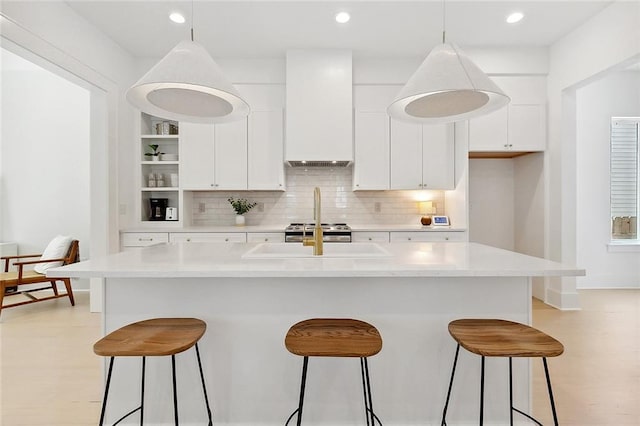 kitchen with a center island with sink, pendant lighting, white cabinetry, and custom range hood