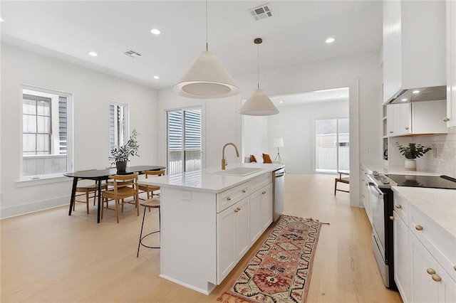 kitchen featuring white cabinetry, stainless steel appliances, ventilation hood, an island with sink, and pendant lighting