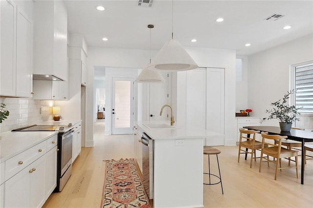 kitchen with stainless steel appliances, a kitchen island with sink, sink, white cabinets, and hanging light fixtures