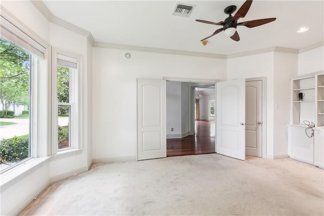 unfurnished bedroom with a ceiling fan, light colored carpet, baseboards, ornamental molding, and visible vents
