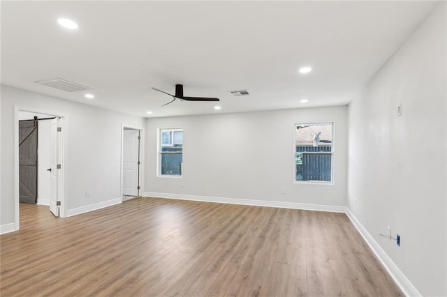 spare room featuring a barn door, ceiling fan, light hardwood / wood-style flooring, and a healthy amount of sunlight