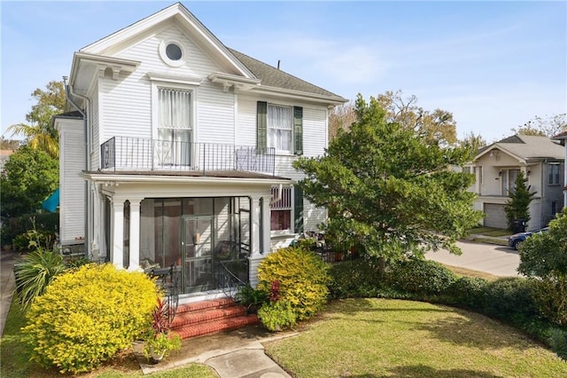 view of front facade with a front yard, a balcony, and a sunroom