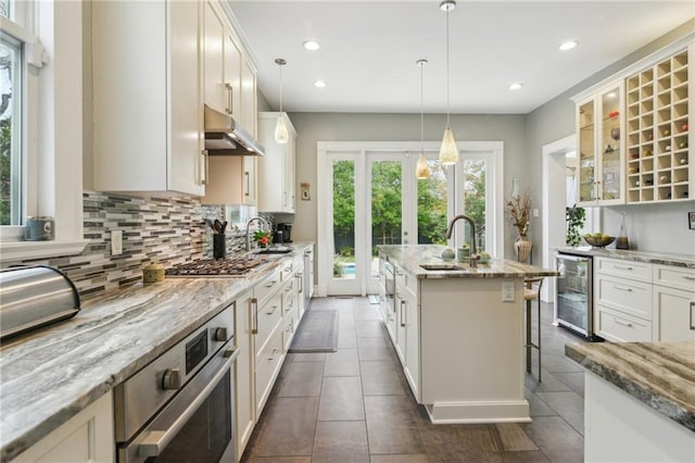 kitchen featuring a kitchen breakfast bar, appliances with stainless steel finishes, beverage cooler, and light stone counters