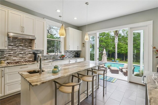 kitchen with light stone countertops, pendant lighting, white cabinets, backsplash, and stainless steel gas cooktop