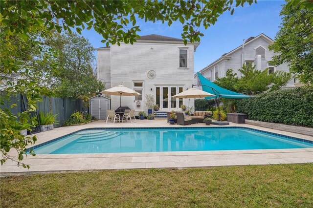 view of pool with outdoor lounge area, a patio, a lawn, and a storage unit