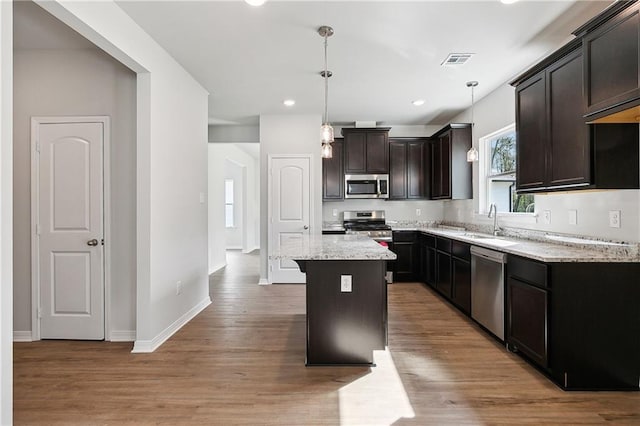 kitchen featuring stainless steel appliances, wood-type flooring, a kitchen island, pendant lighting, and light stone counters