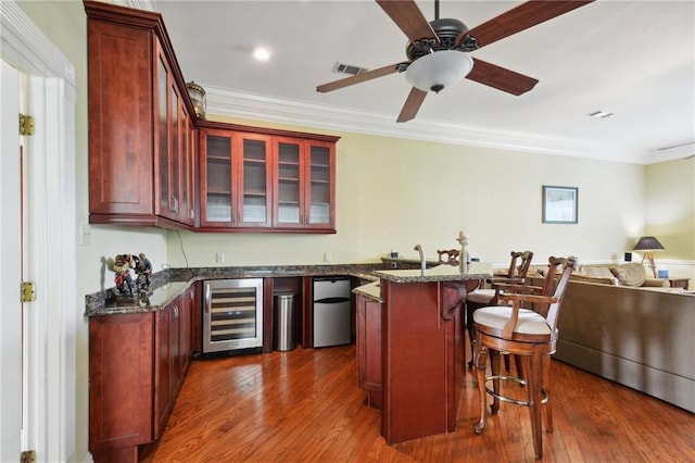 bar featuring dark wood-type flooring, beverage cooler, dark stone countertops, crown molding, and refrigerator