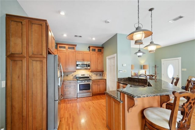 kitchen with sink, hanging light fixtures, light hardwood / wood-style flooring, dark stone counters, and appliances with stainless steel finishes