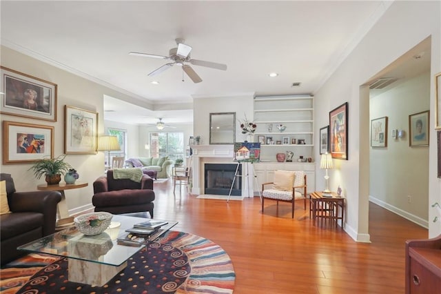 living room featuring hardwood / wood-style floors, ceiling fan, built in features, and crown molding