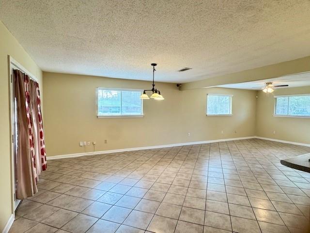 tiled spare room with ceiling fan with notable chandelier and a textured ceiling