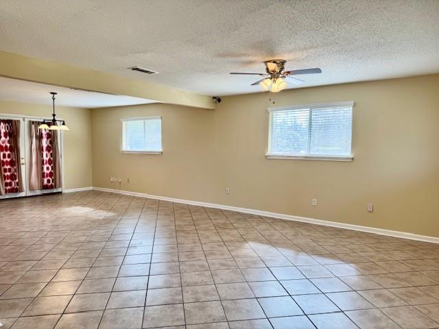 tiled empty room featuring ceiling fan, a healthy amount of sunlight, and a textured ceiling