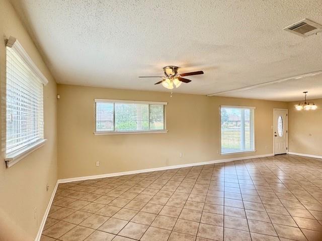 empty room featuring light tile patterned floors, a healthy amount of sunlight, and ceiling fan with notable chandelier