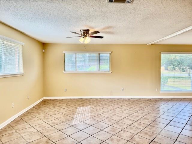 empty room with ceiling fan, light tile patterned flooring, and a textured ceiling