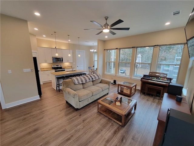 living room featuring ceiling fan with notable chandelier, sink, and hardwood / wood-style floors