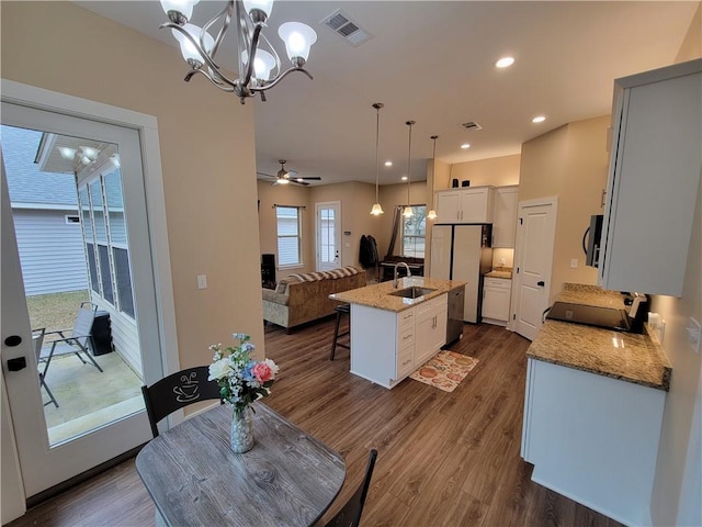 kitchen featuring sink, white cabinetry, decorative light fixtures, an island with sink, and light stone countertops