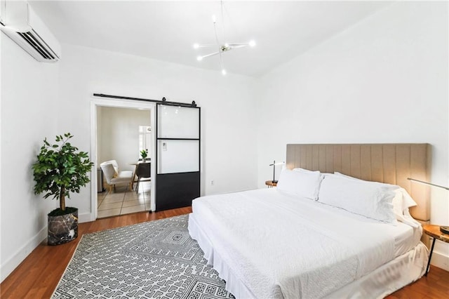 bedroom with a wall mounted air conditioner, a barn door, hardwood / wood-style flooring, and a notable chandelier