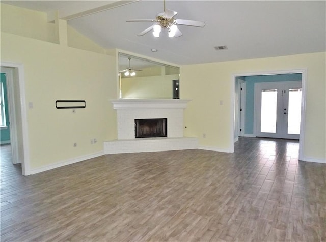 unfurnished living room with french doors, a brick fireplace, ceiling fan, wood-type flooring, and vaulted ceiling with beams