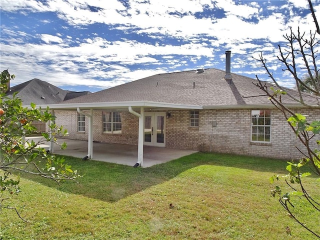 back of property with brick siding, roof with shingles, a lawn, french doors, and a patio area