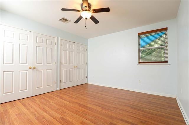 unfurnished bedroom with multiple closets, ceiling fan, and light wood-type flooring