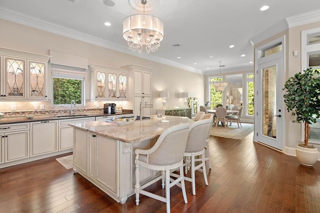 kitchen featuring a center island, sink, hanging light fixtures, light stone counters, and crown molding