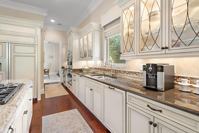 kitchen with tasteful backsplash, dark stone counters, crown molding, sink, and stainless steel gas stovetop