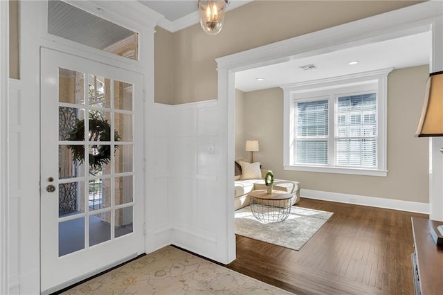 living area with baseboards, wood finished floors, visible vents, and crown molding