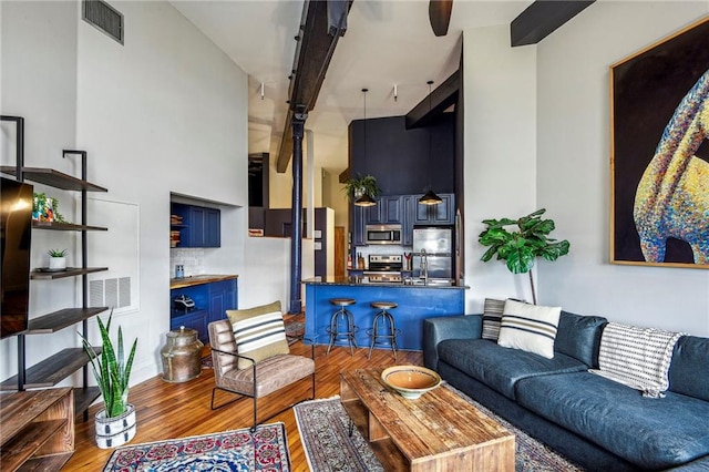 living room with a high ceiling, beamed ceiling, wood finished floors, and visible vents