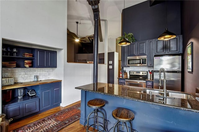 kitchen featuring blue cabinets, stainless steel appliances, wood finished floors, dark stone counters, and tasteful backsplash