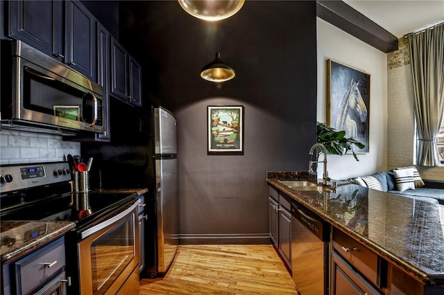 kitchen featuring light wood-style flooring, dark stone countertops, a sink, stainless steel appliances, and backsplash