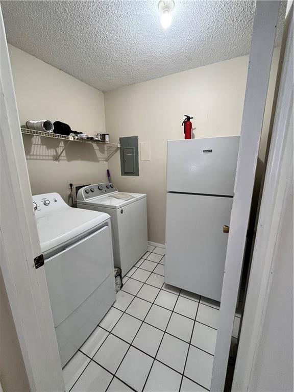 laundry room with a textured ceiling, light tile patterned floors, electric panel, and washer and clothes dryer