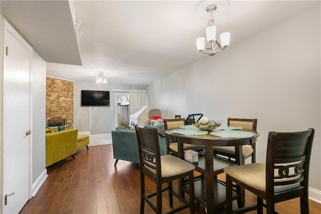 dining area with a chandelier, dark hardwood / wood-style flooring, and a brick fireplace