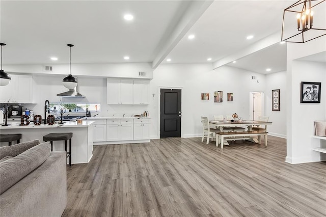 kitchen featuring an inviting chandelier, light wood-type flooring, vaulted ceiling with beams, white cabinetry, and decorative light fixtures