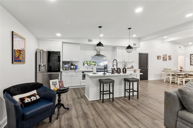 kitchen featuring white cabinetry, a kitchen breakfast bar, hanging light fixtures, stainless steel fridge, and a kitchen island with sink