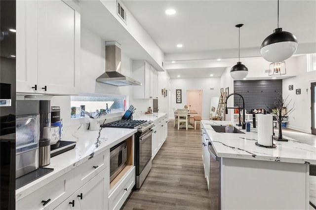 kitchen with sink, stainless steel appliances, white cabinets, wall chimney exhaust hood, and hanging light fixtures