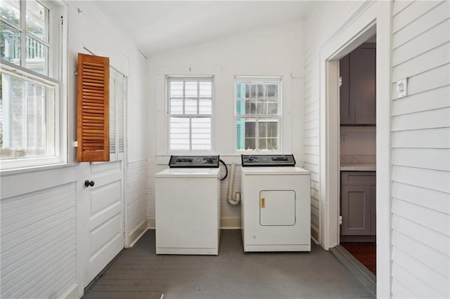 laundry room featuring separate washer and dryer, plenty of natural light, and wood walls