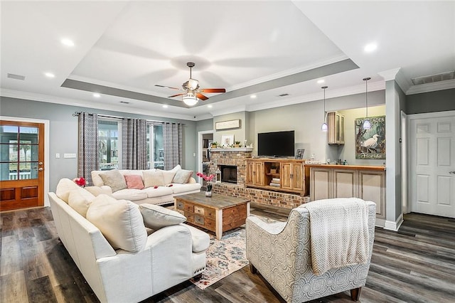 living room with a tray ceiling, ceiling fan, a fireplace, and dark wood-type flooring