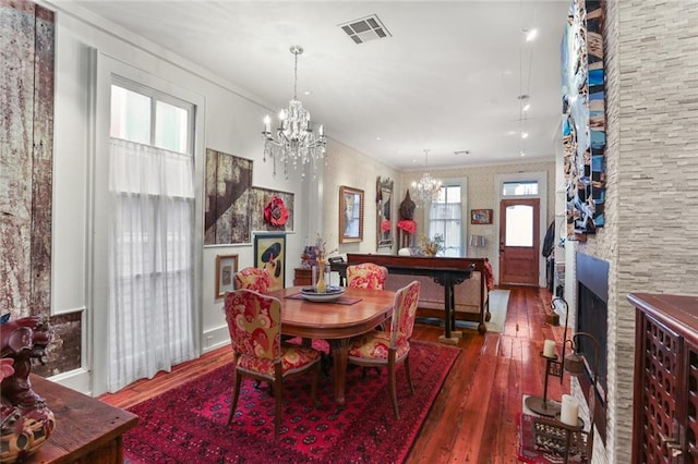 dining area with a stone fireplace, crown molding, dark wood-type flooring, and an inviting chandelier