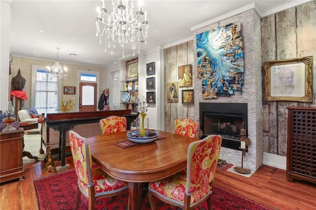 dining area featuring crown molding, a fireplace, wood-type flooring, and an inviting chandelier