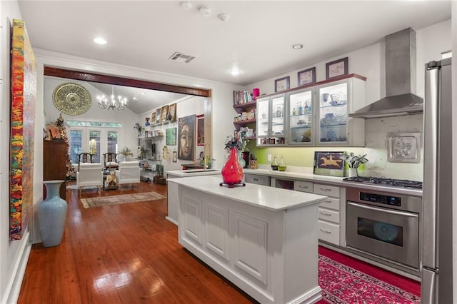 kitchen featuring white cabinets, wall chimney exhaust hood, stainless steel appliances, and a kitchen island