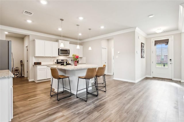 kitchen featuring stainless steel appliances, pendant lighting, light hardwood / wood-style flooring, white cabinetry, and an island with sink